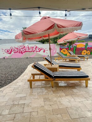 Seients de relax a l'aire lliure amb coixins estampats, un para-sol vermell i un mural amb cactus i flors.