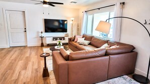 A modern living room with a brown leather sofa, a flat-screen TV, a floor lamp, and a small side table. -  Resort-Style Oasis Near Old Town Scottsdale (Scottsdale)