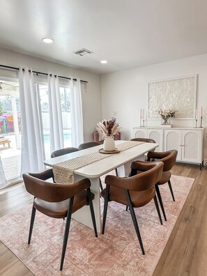 A dining area with a white table, brown chairs, a white cabinet, and a large window with curtains. - Old Town Scottsdale Getaway! Heated Pool + Hot Tub -4BR (Scottsdale)