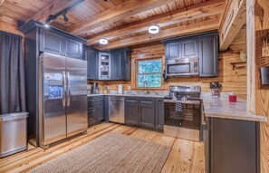 A modern kitchen with stainless steel appliances, wooden cabinetry, and a large window.