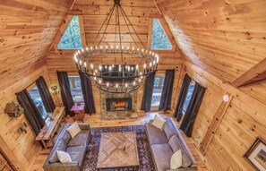 Ein gemütliches Blockhauskaminzimmer mit Kamin, Holzwänden, einer Chandelierleuchtre und einer Sitzecke.
