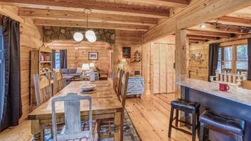 A wooden cabin interior with a dining area, bar, and kitchen.