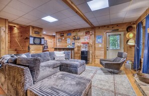 Ein gemütliches Blockhaus-Interieur mit einer Eckcouch, einem Sessel, einer kleinen Bar und einer Tür, die nach draußen führt.