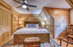 Ein Schlafzimmer einer Holzhütte mit einem Bett, einer Kommode, einem Sessel und einem Deckenventilator.