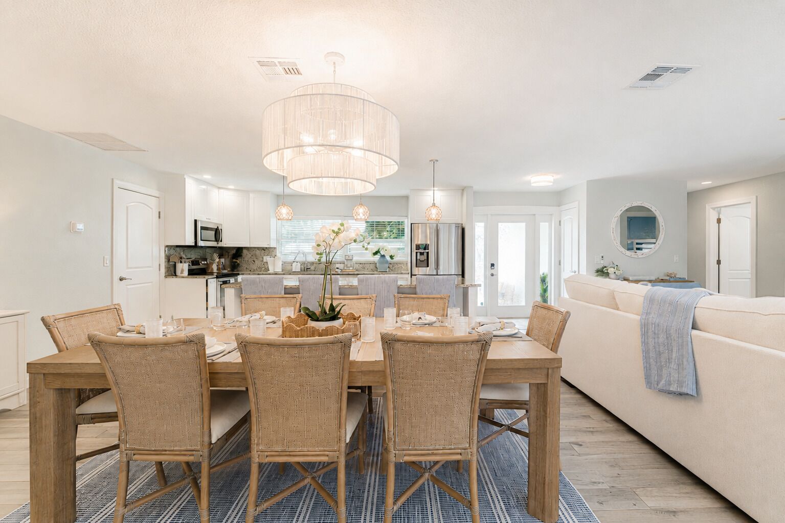 A modern kitchen with white cabinets, a dining area with wicker chairs, and a large chandelier.