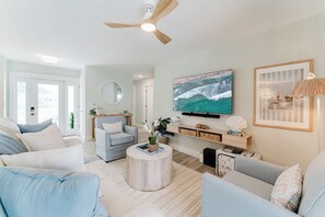 Ein Wohnzimmer mit Deckenventilator, einem Wand-Fernseher, einem runden Couchtisch und einem Sofa.