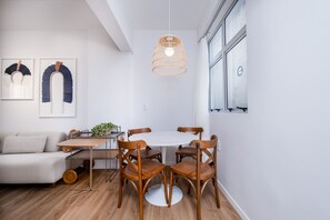 A modern dining area with a round table and wooden chairs, a hanging light fixture, and a white wall with framed artwork. - Modern Apartment in the Center of Floripa Vlr301 (Florianópolis)