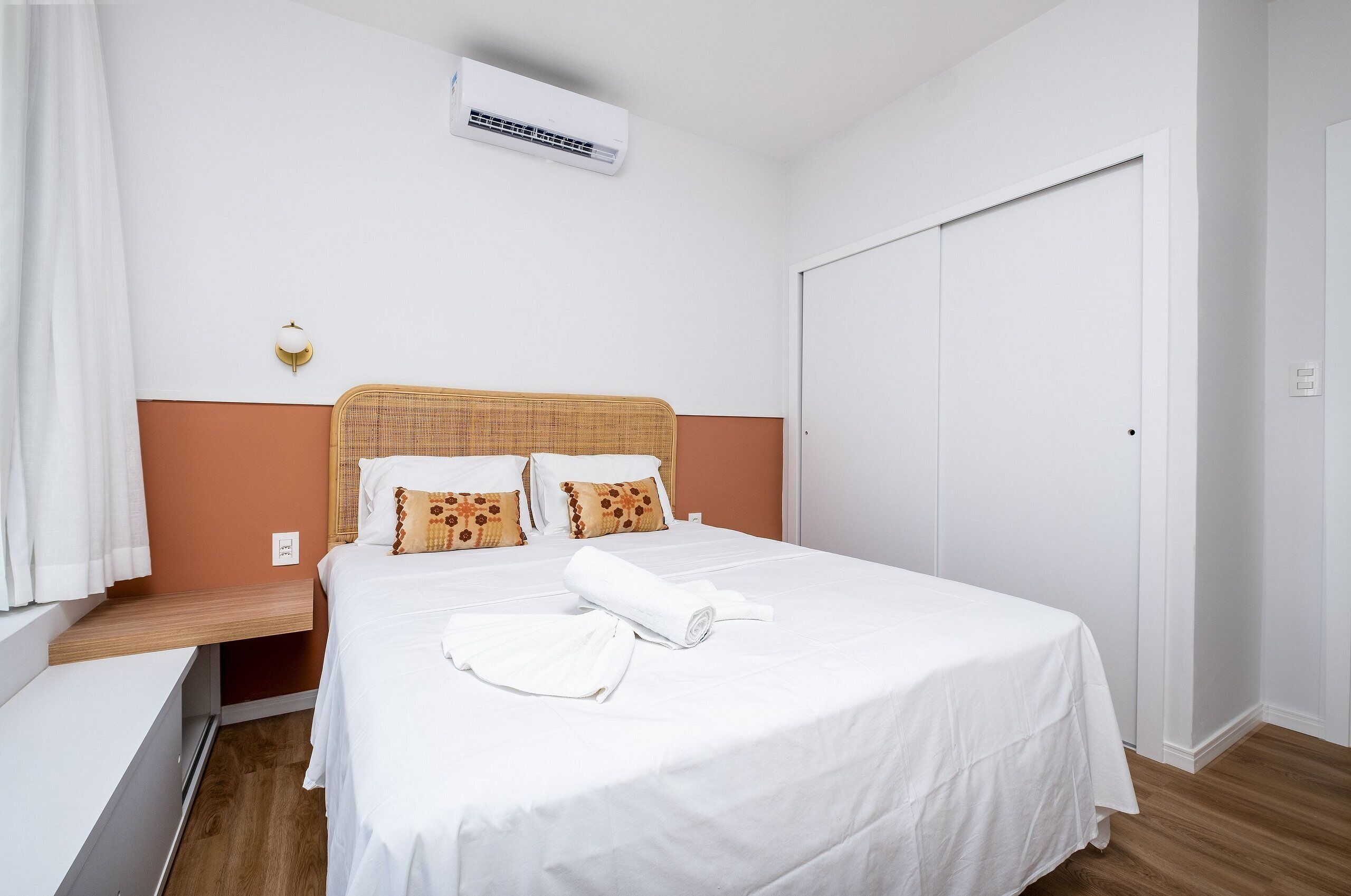 A neatly made bed with white bedding, a wooden headboard, and two pillows with brown and orange patterns.