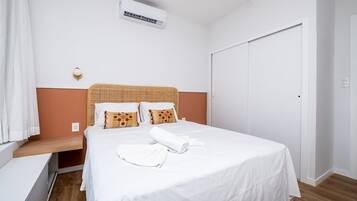 A neatly made bed with white bedding, a wooden headboard, and two pillows with brown and orange patterns.