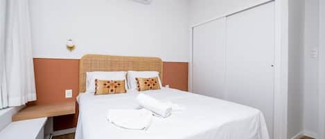 Una cama bien hecha con ropa blanca, cabecera de madera y dos almohadas con diseños marrones y anaranjados.