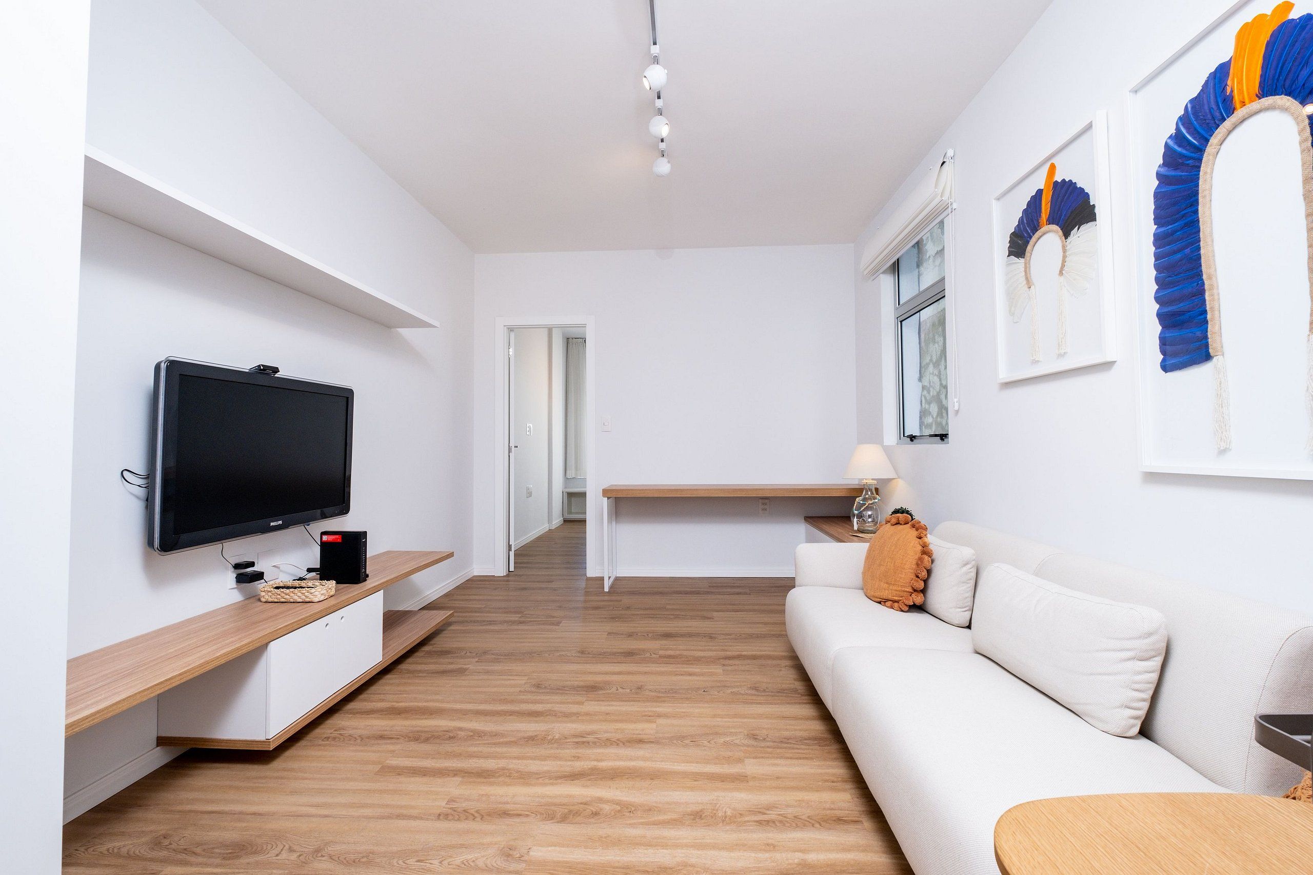 A modern living room with a flat-screen TV, wooden flooring, a white sofa, and a desk with a lamp.