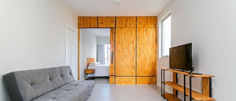 Una sala de estar moderna con un sofá gris, paneles de madera, un televisor sobre un mueble de madera y un ventanal que proporciona luz natural.