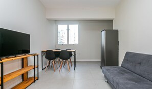 A compact living space with a flat-screen TV on a wooden stand, a gray sofa, a dining table with four chairs, and a refrigerator. - Comfortable apt the Center of Florianopolis Vlr801 (Florianópolis)