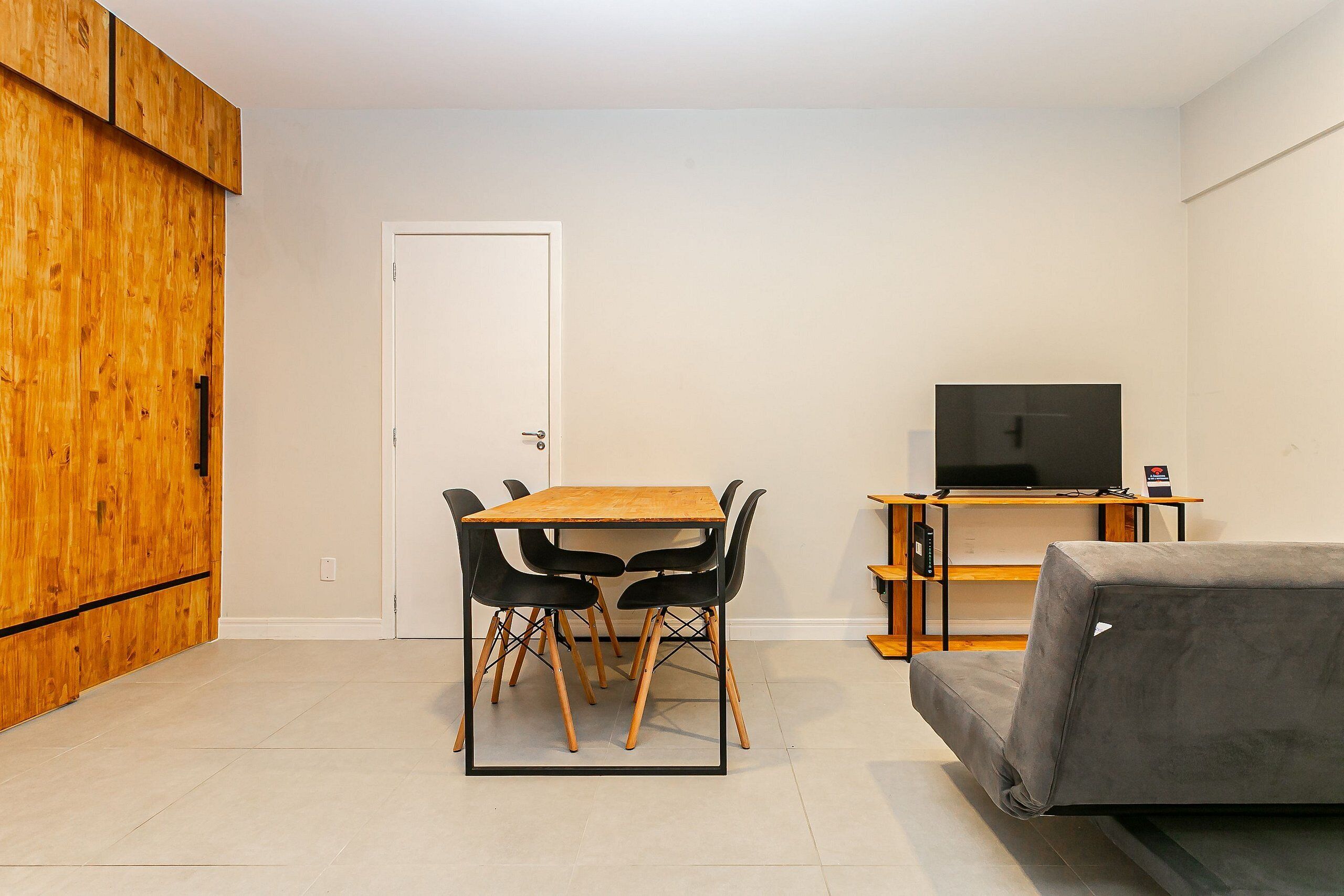 Een gezellig, compact leefruimte met een houten kast, een eettafel met stoelen, een bank en een televisie op een standaard.