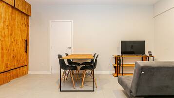 A compact living space with a wooden cabinet, a dining table with chairs, a sofa, and a TV on a stand.