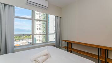 A hotel room with a large bed, a wooden nightstand, and a view of buildings and mountains through the window.