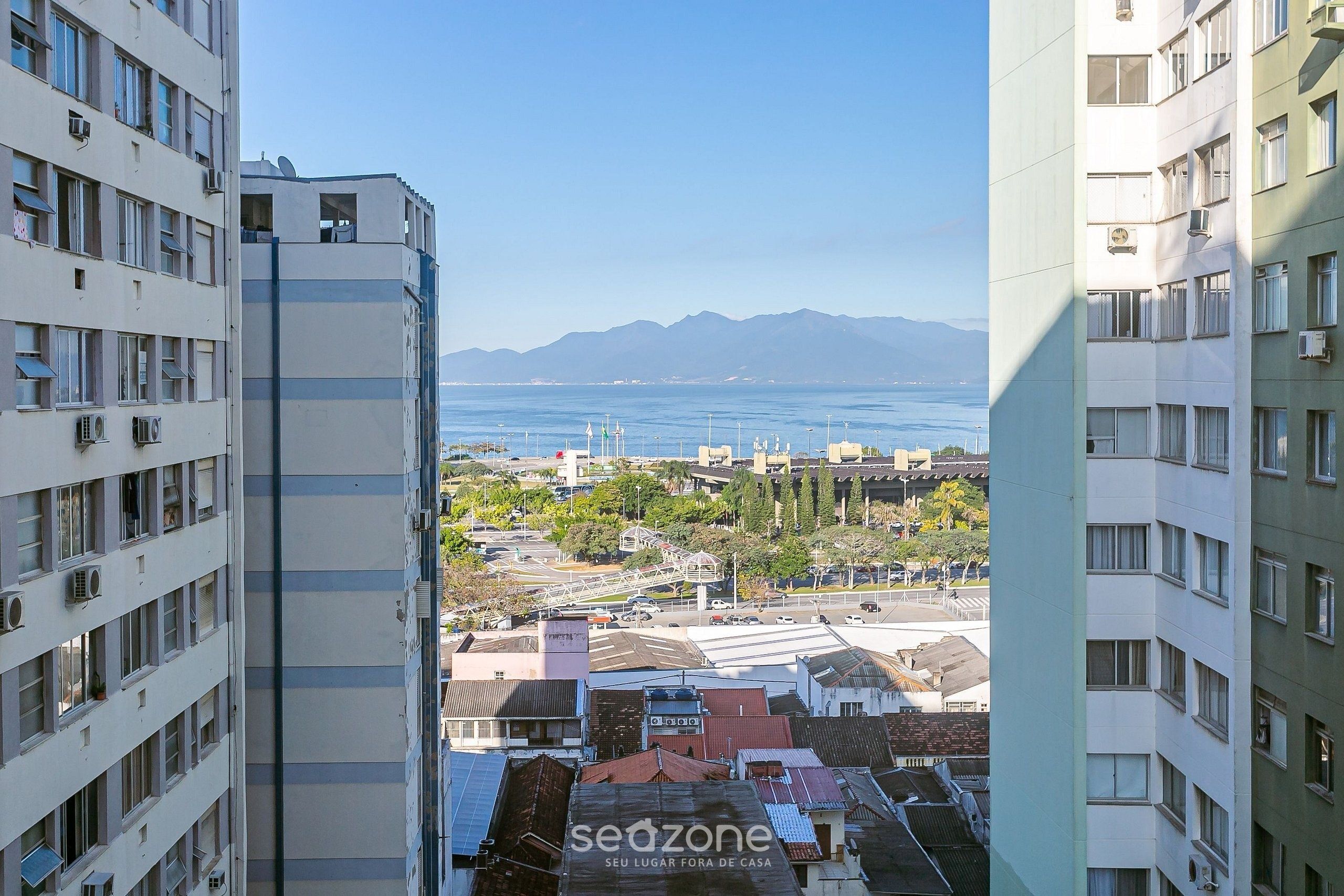 A high-rise building with multiple balconies and a view of a coastal area with mountains in the distance.