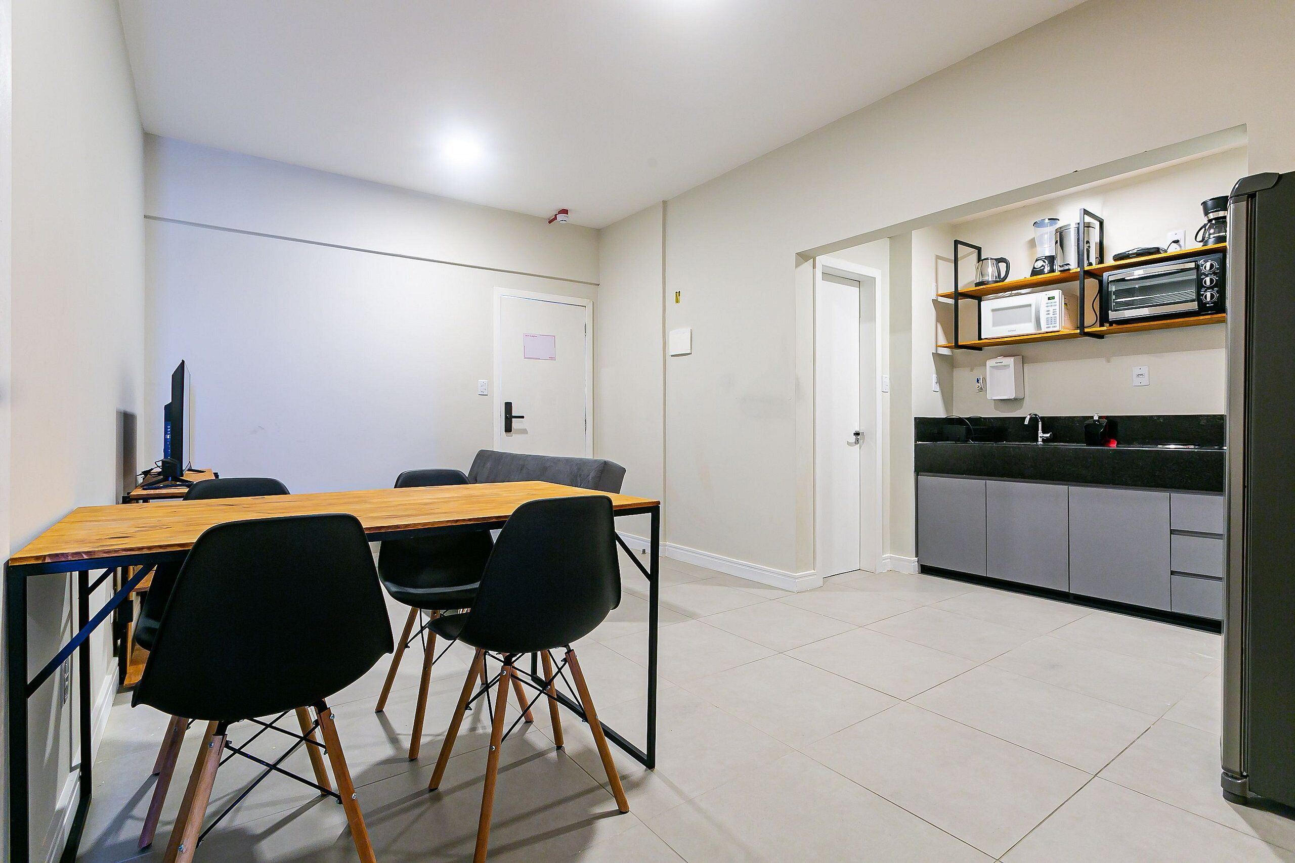 A modern kitchen with a wooden dining table, black chairs, and a built-in microwave.