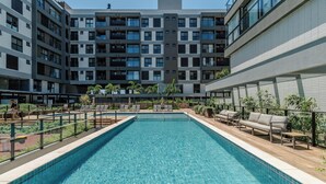Ein Swimmingpool mit Liegestühlen und Blick auf ein mehrgeschossiges Gebäude.