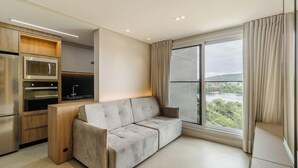 Ein modernes Wohnzimmer mit einer Couch, einer Küchenzeile mit Geräten und einem großen Fenster mit Blick auf eine Landschaft.