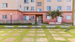 Un edificio residencial de varios pisos con fachada plana, una entrada central y una pequeña área de jardín con palmeras.
