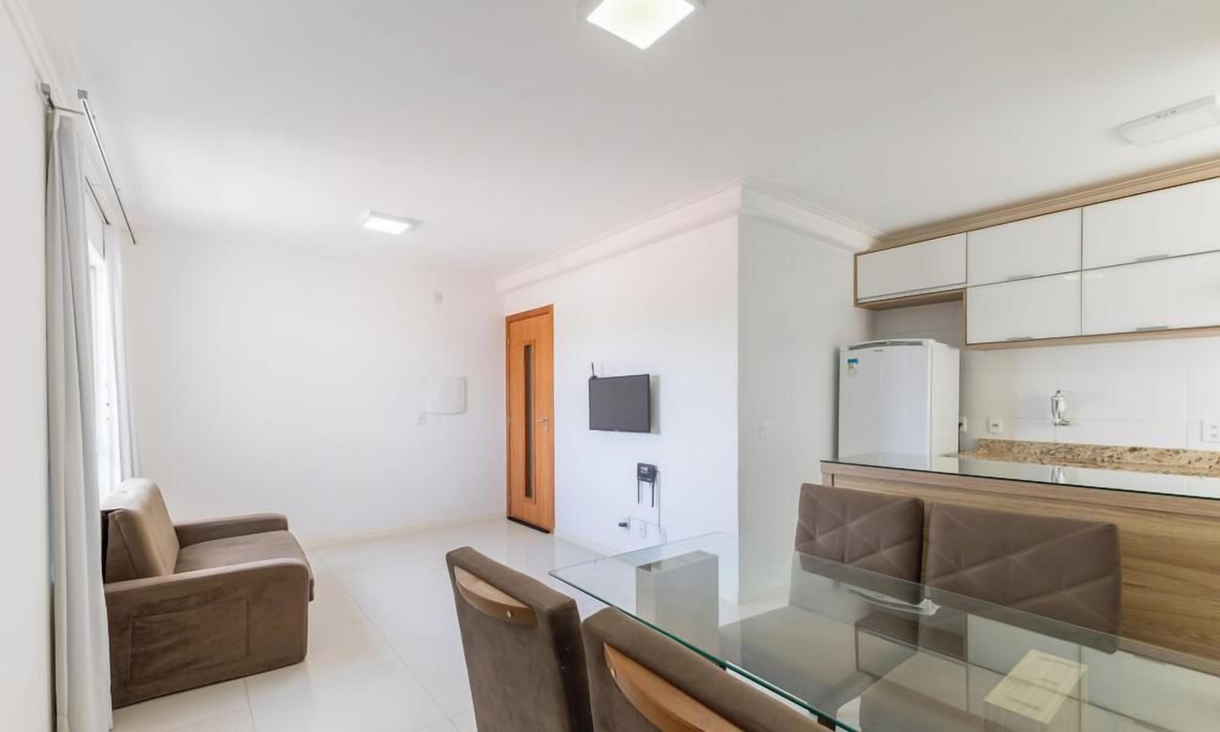 A modern kitchen with a glass dining table, a sofa, and a TV mounted on the wall.