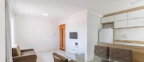 A modern kitchen with a glass dining table, a sofa, and a TV mounted on the wall.