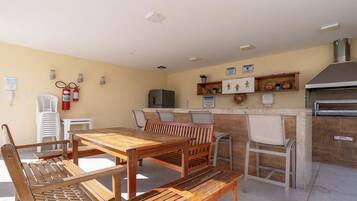 An outdoor kitchen area with a wooden table and chairs, a refrigerator, and a grill.