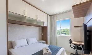 A hotel room with a bed, a desk with a chair, a TV, and a window with a view. - Apt in Condo w/ Pool in S. Francisco Vgt0603 (Ilhéus)