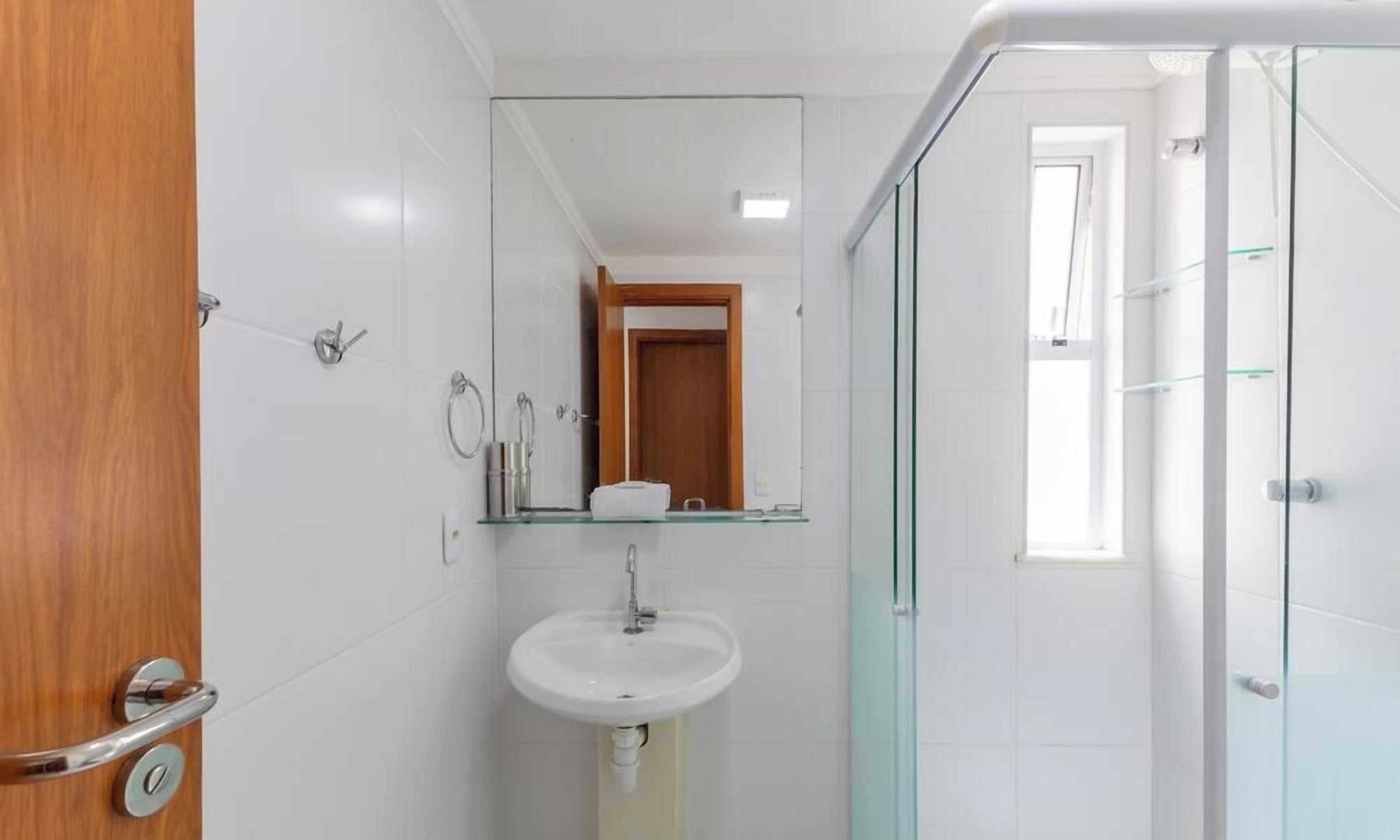 Casa de banho com lavatório branco, espelho e cabine de duche em vidro.
