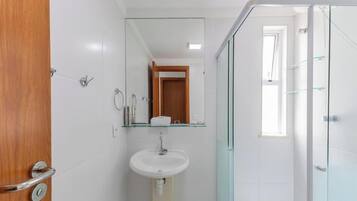 Casa de banho com lavatório branco, espelho e cabine de duche em vidro.