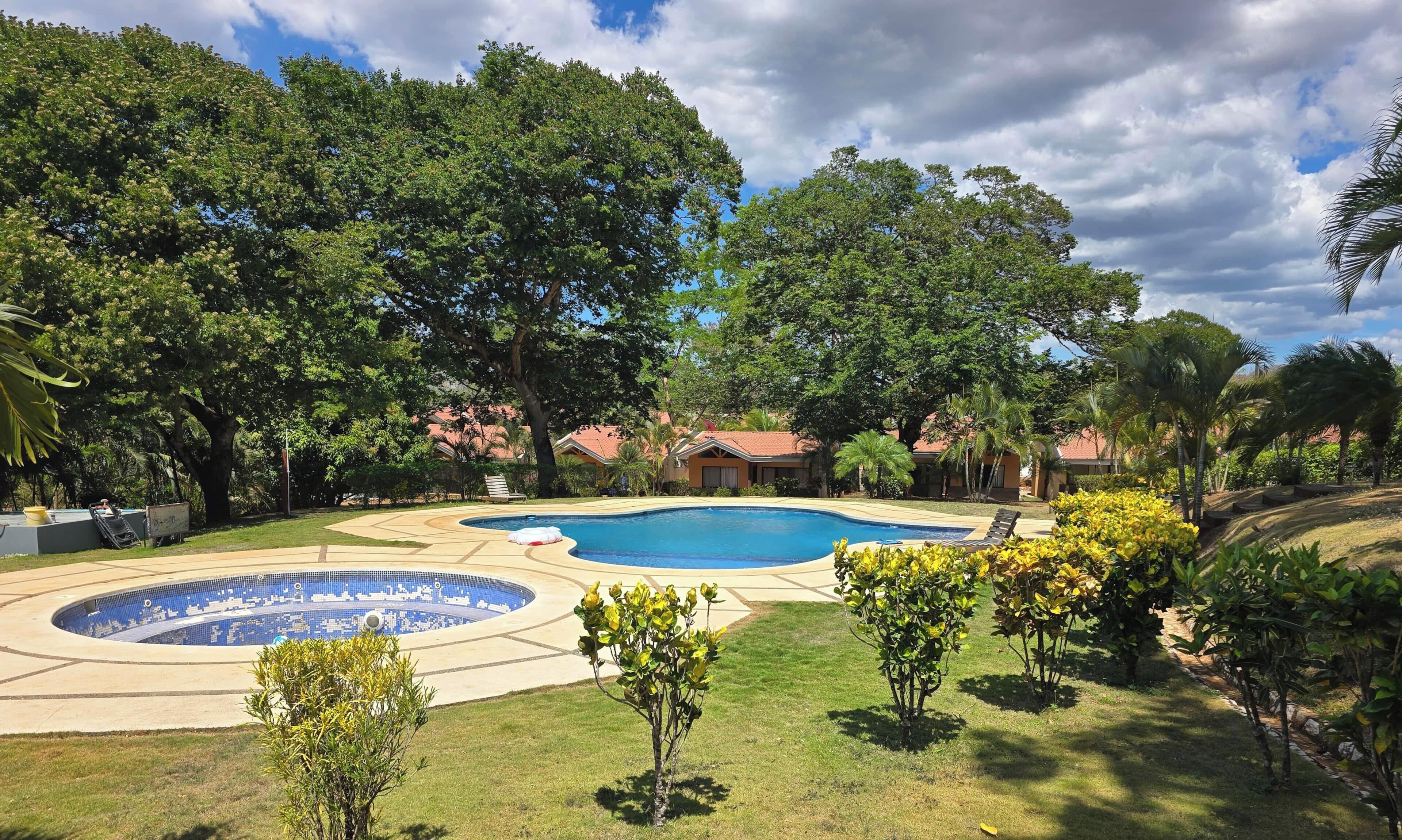 Una piscina con diseño circular, rodeada por un césped cuidado y varios árboles.