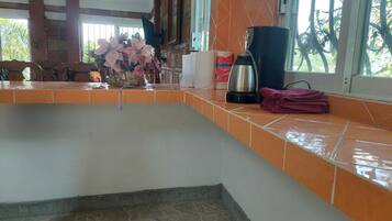 A kitchen with a tiled countertop, a coffee maker, and a window with a view of greenery.