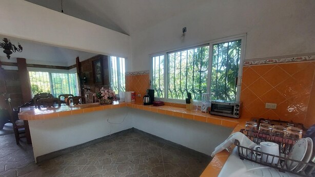 A kitchen with a stone floor, a sink, a dishwasher, and a window with a view of greenery. - Tranquil 3-bedroom house in joyas de agua  perfect for relaxing courtesy coffee (Emiliano Zapata)