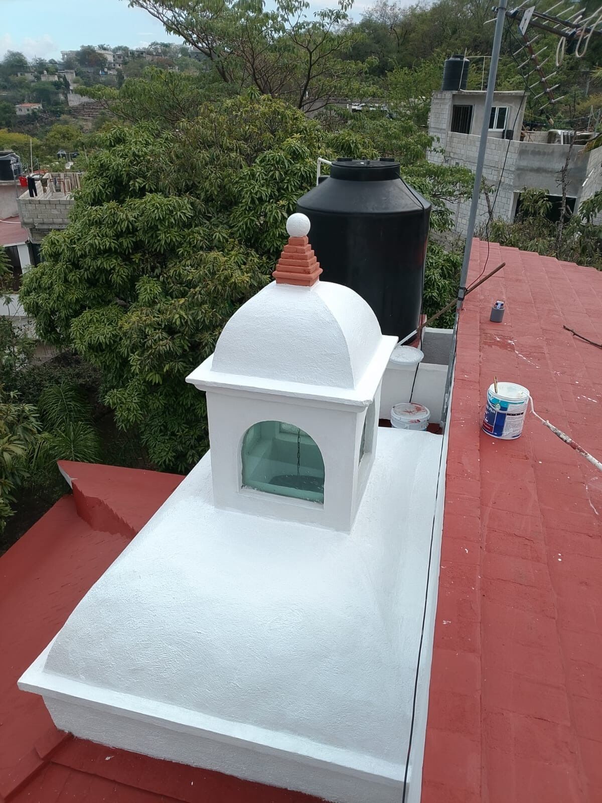 Un toit-terrasse surmonté d’une structure en forme de dôme blanc, d’un réservoir d’eau noir et d’un toit rouge.