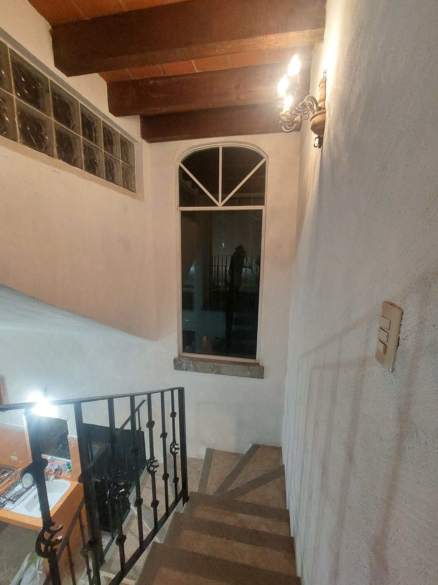 A staircase with a handrail, a window with a decorative frame, and a wall-mounted light fixture.