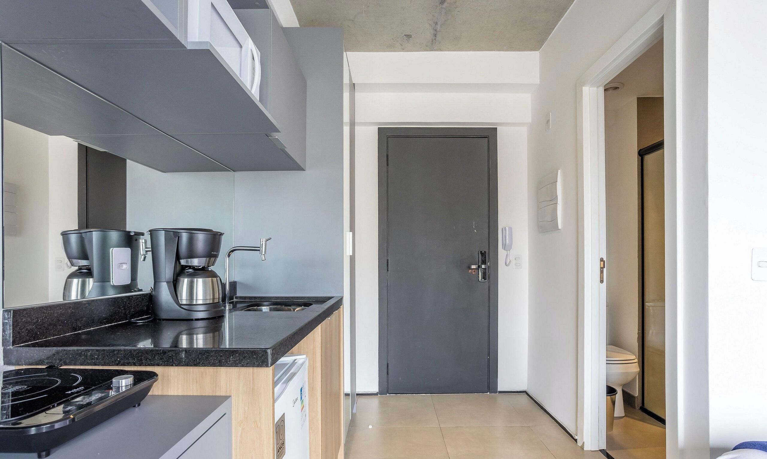 A modern kitchen with a stove, coffee maker, and a door leading to a bathroom.