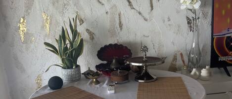 A round table with a white tablecloth, surrounded by chairs, a potted plant, a decorative bowl, and a vase with white flowers.