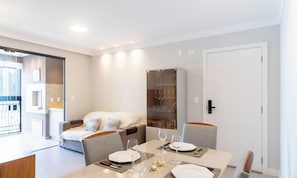 Una habitación de hotel moderna con zona de comedor, un sofá y un aparador de vidrio.