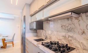 Una cocina moderna con estufa a gas, pileta de acero inoxidable y salpicadero de mármol.