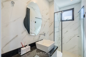 Un baño moderno con un espejo grande, un lavamanos blanco y una cabina de ducha de vidrio.
