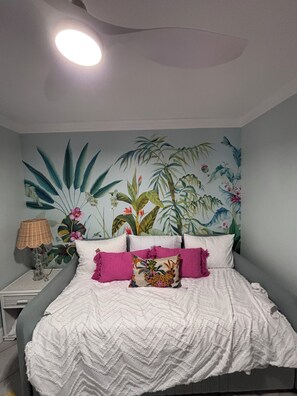 Ein Schlafzimmer mit einem Bett, Kissen, einem Nachttisch, einer Lampe und Wandbild.