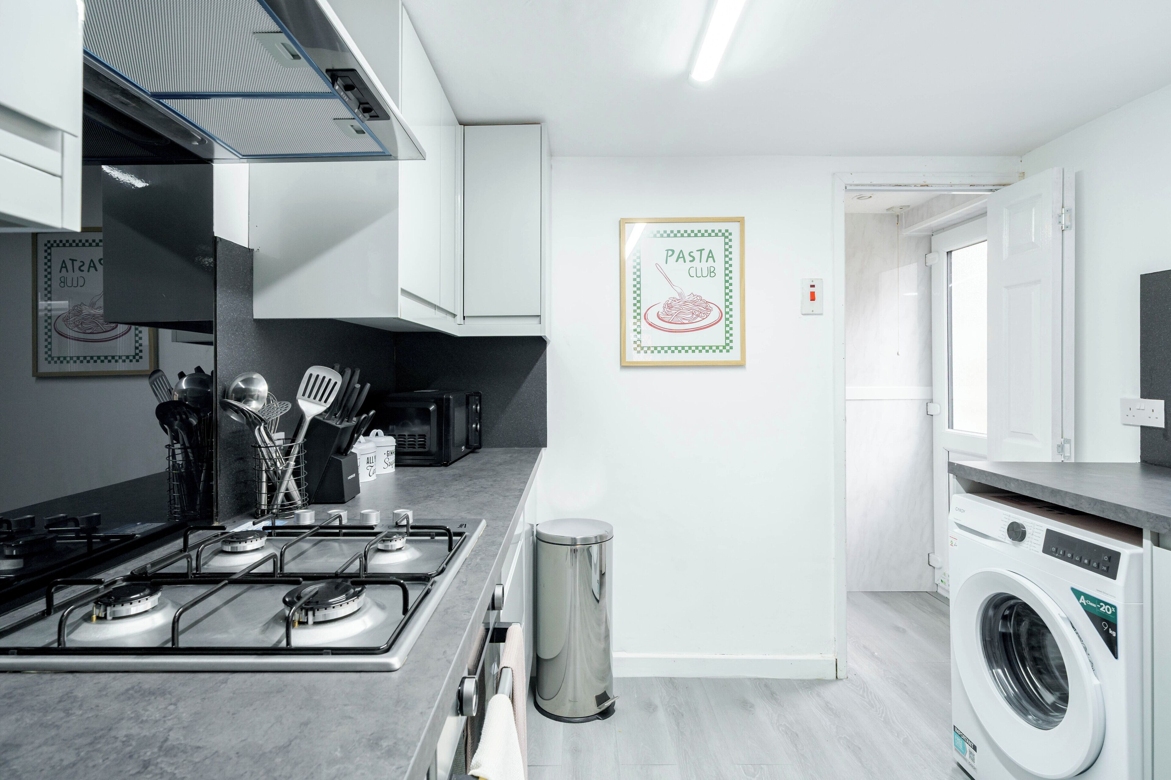 Una cocina moderna con estufa a gas, electrodomésticos de acero inoxidable y un cartel enmarcado del club de pasta en la pared.