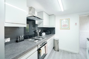 A modern kitchen with a gas stove, oven, and microwave. There is a trash bin and a framed picture on the wall. - Sleeps 5, Free Parking, Stylish Spacious Home (Kingston upon Hull)