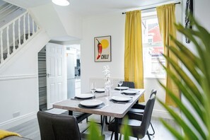 A dining area with a table set for four, a staircase, and a kitchen in the background. - Sleeps 5, Free Parking, Stylish Spacious Home (Kingston upon Hull)