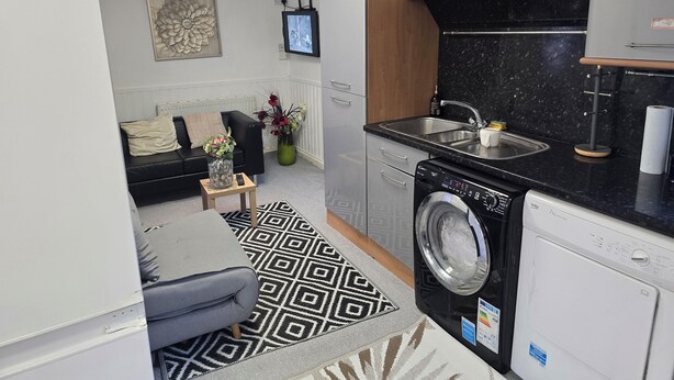 A compact kitchen with a washing machine, a sink, and a television. - Private & Charming Annex. Wi-Fi, Free parking, 15 min to Swindon Designer shops. (Highworth)