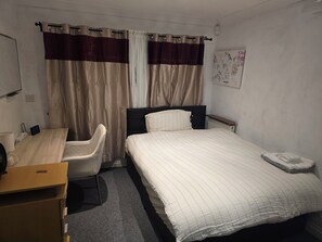 Una habitación de hotel con cama, escritorio, silla, radiador y un reloj de pared.