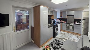 A modern kitchen with built-in appliances, a washing machine, and a dining area with a patterned rug. - Private & Charming Annex. Wi-Fi, Free parking, 15 min to Swindon Designer shops. (Highworth)