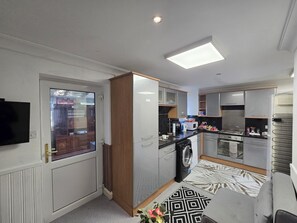 A modern kitchen with built-in appliances, a washing machine, and a dining area with a patterned rug. - Private & Charming Annex. Wi-Fi, Free parking, 15 min to Swindon Designer shops. (Highworth)