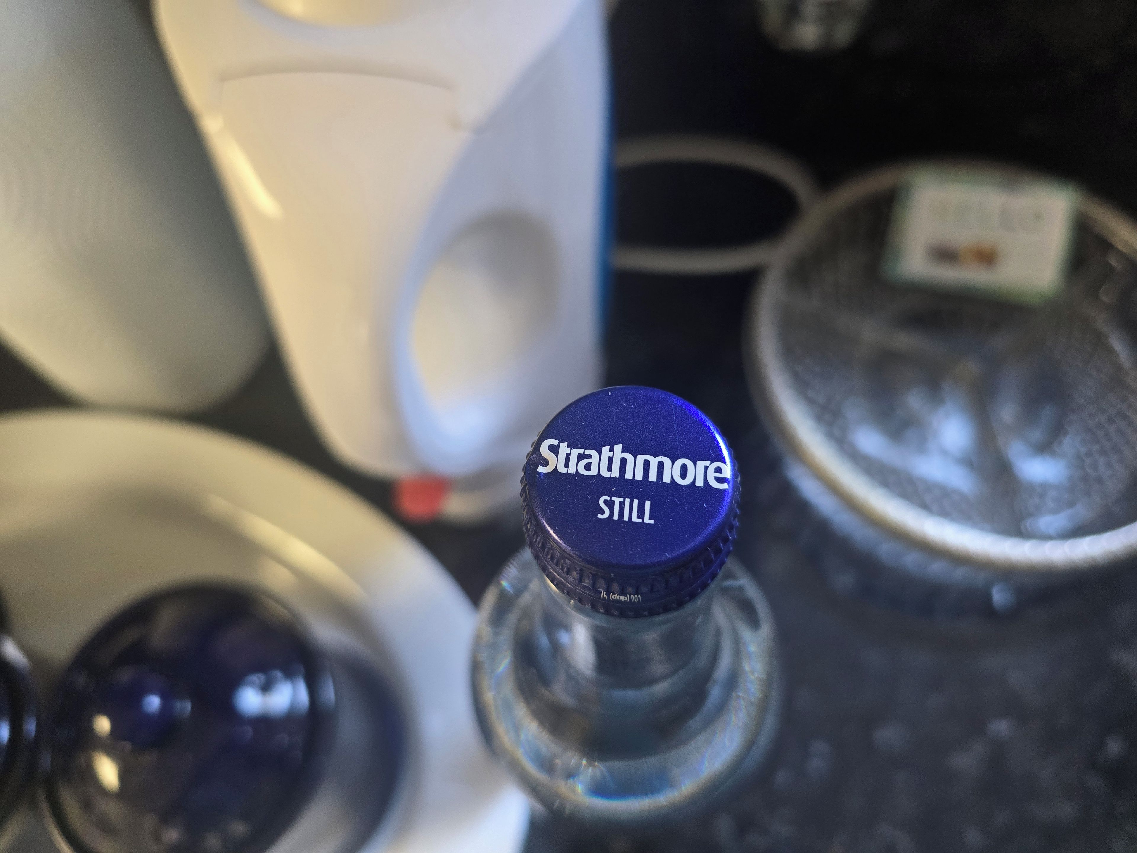 Eine Flasche mit blauem Verschluss, beschriftet mit 'Strathmore STILL', und eine weiße Tasse im Hintergrund.